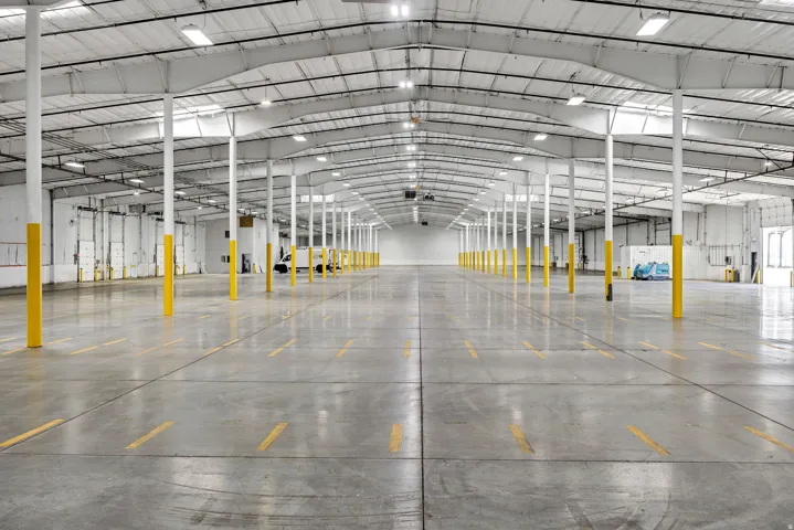 Expansive warehouse space featuring polished concrete flooring, high ceilings with exposed trusses, numerous support columns, multiple dock doors, and abundant overhead lighting