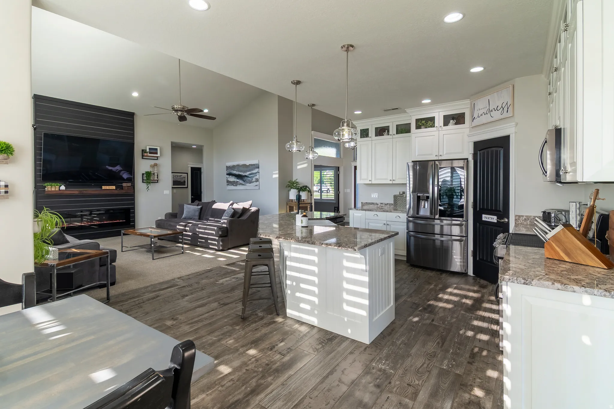Open-concept living space featuring vaulted ceilings, wood-finish flooring, a kitchen island with pendant lighting, white cabinetry, and stainless steel appliances