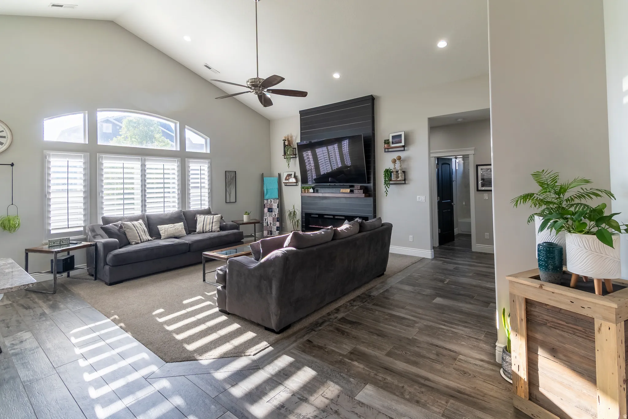 Vaulted ceilings enhancing the living area, featuring wood-finish flooring, a contemporary ceiling fan, and a fireplace with a dark-paneled surround