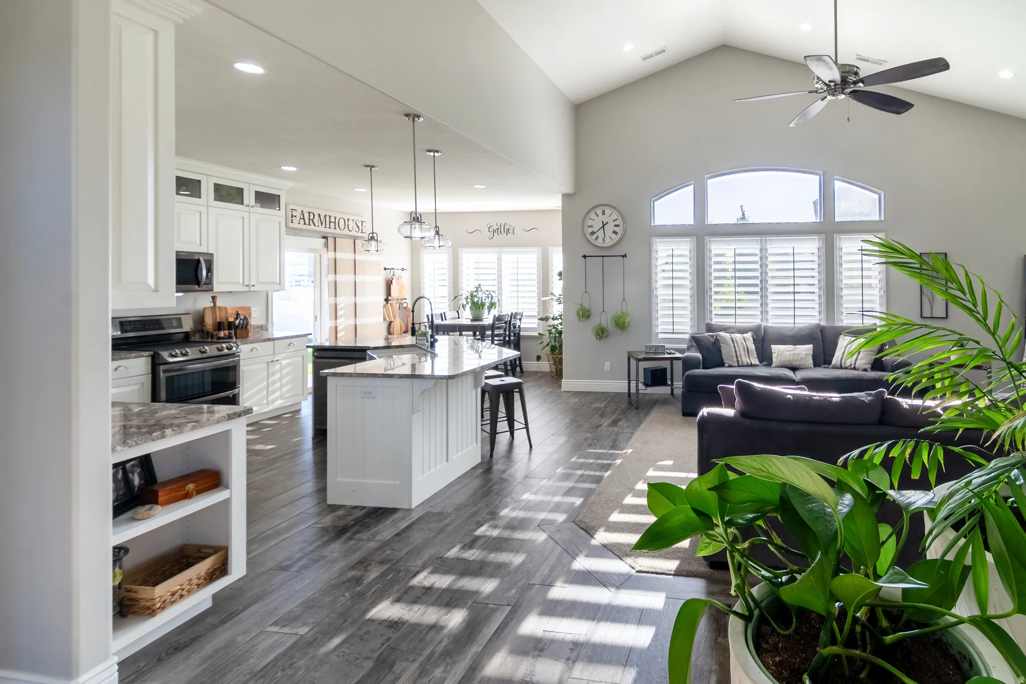 Open-concept living space featuring vaulted ceilings, wood-finish flooring, and white plantation shutters