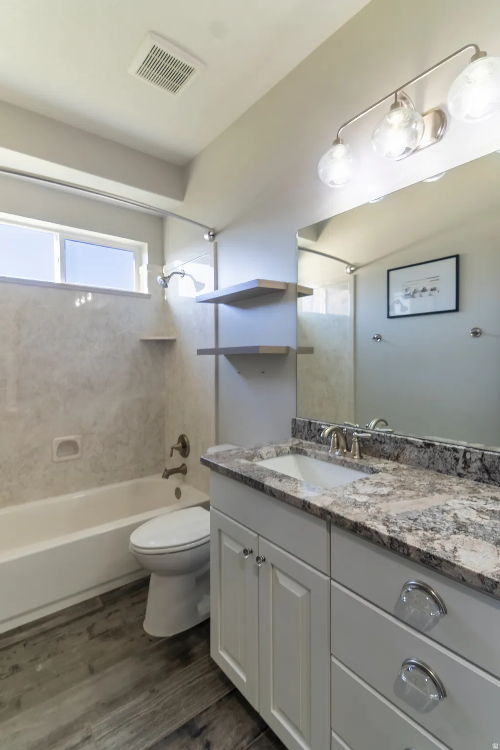 Updated bathroom featuring a single vanity with stone-finish countertop, undermount sink, and light wood-finish flooring