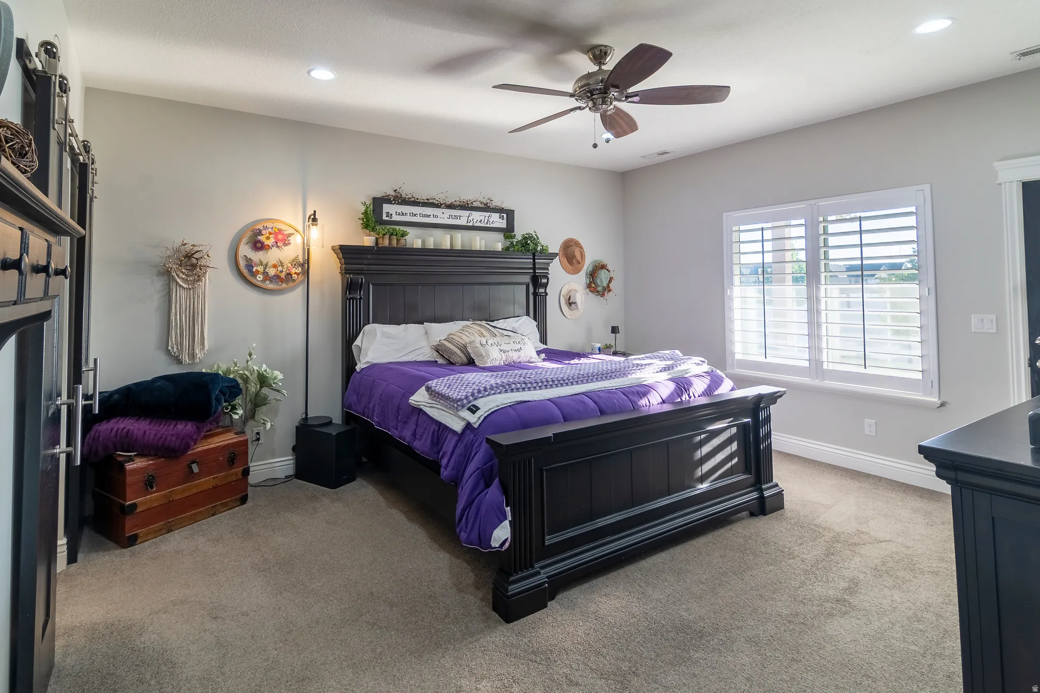Carpeted room featuring light gray walls, a ceiling fan with integrated lighting, recessed lighting, and a large window with white plantation shutters