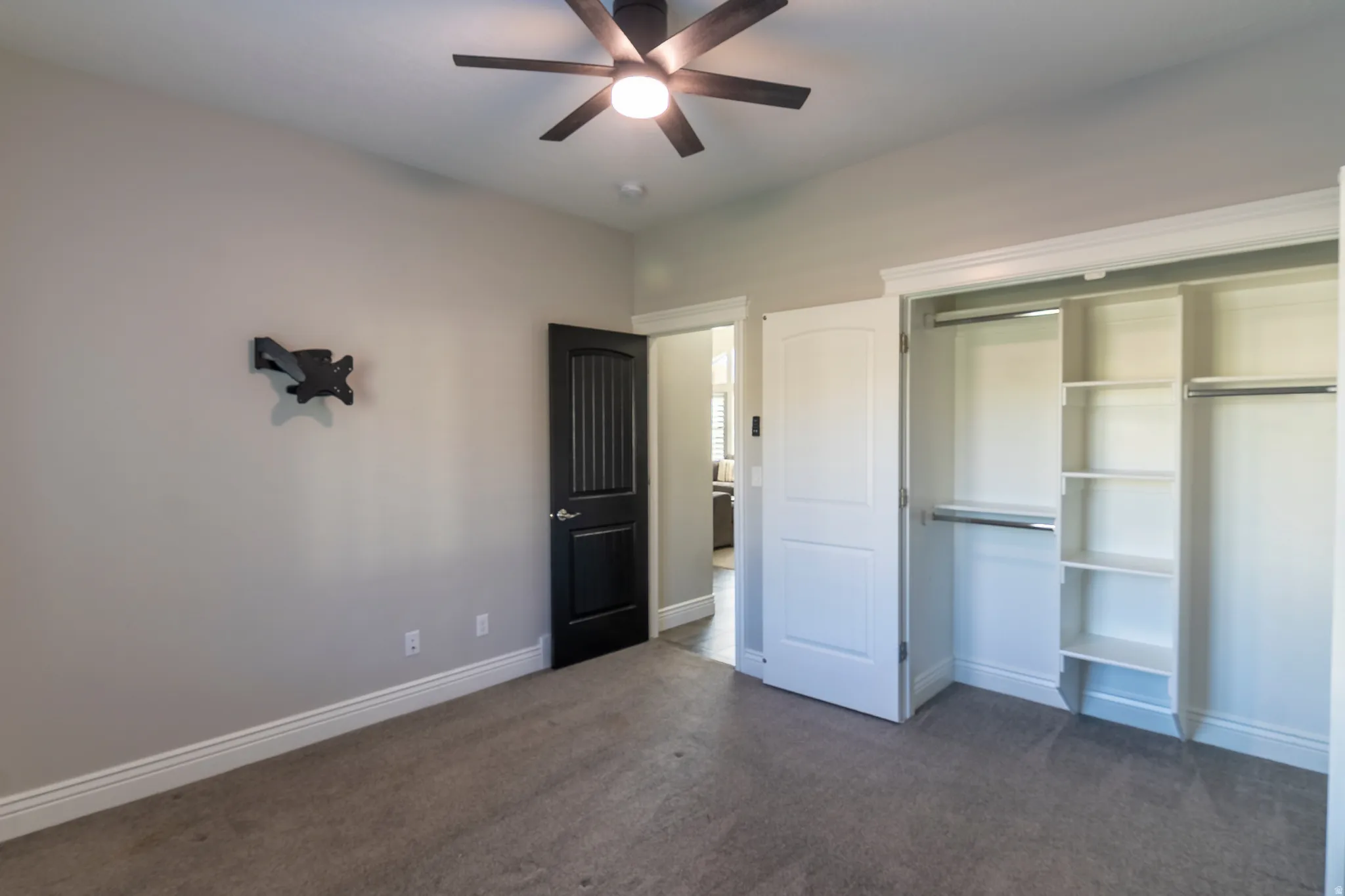 Carpeted room featuring a ceiling fan with integrated lighting, a black paneled door, and a built-in closet with shelving and hanging rods