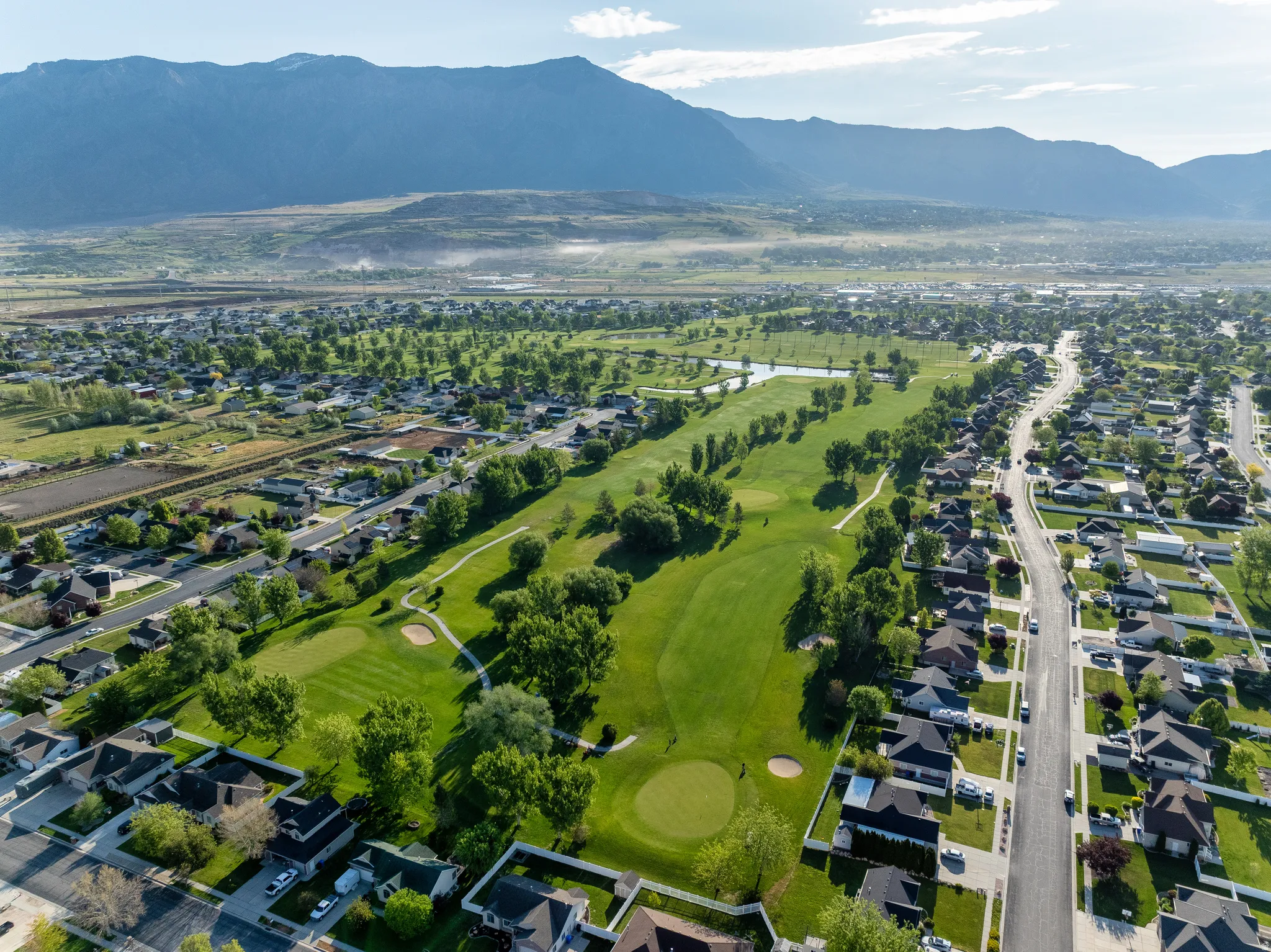 Expansive aerial perspective showcasing a residential community bordering a golf course with mature trees and water features