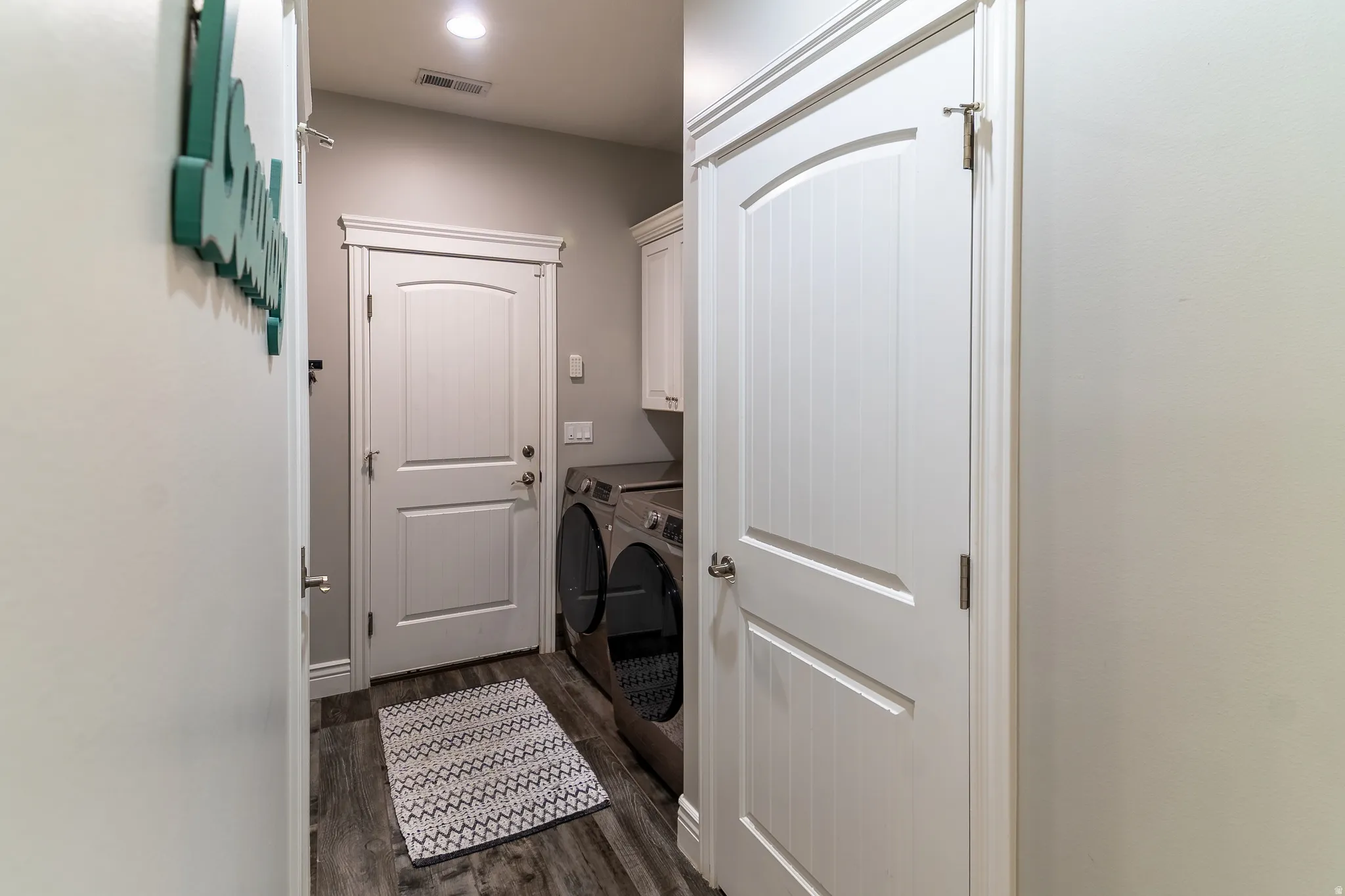 Laundry area featuring wood-finish flooring, white cabinetry, a recessed light fixture, and white interior doors with decorative trim