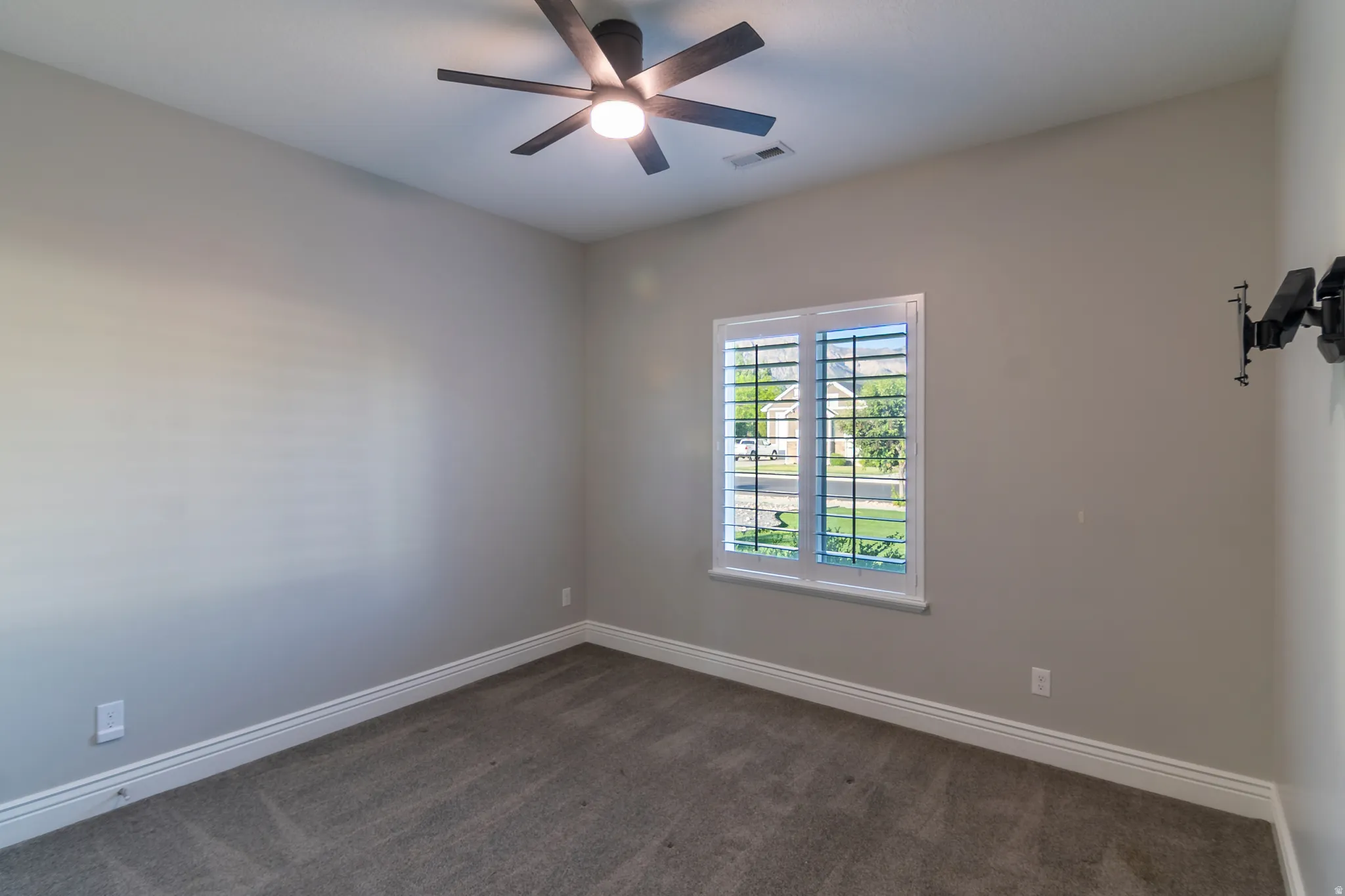 Bedroom featuring a ceiling fan with integrated lighting, a window with plantation shutters, neutral-toned walls, and grey carpeting