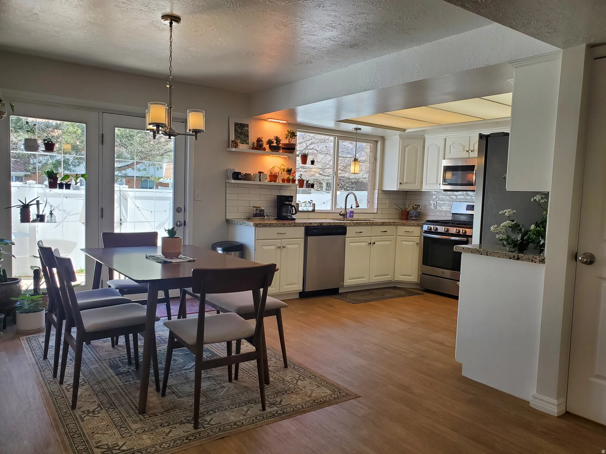 Open-concept kitchen and dining area featuring light wood-finish flooring, white cabinetry, stainless steel appliances, and a subway tile backsplash