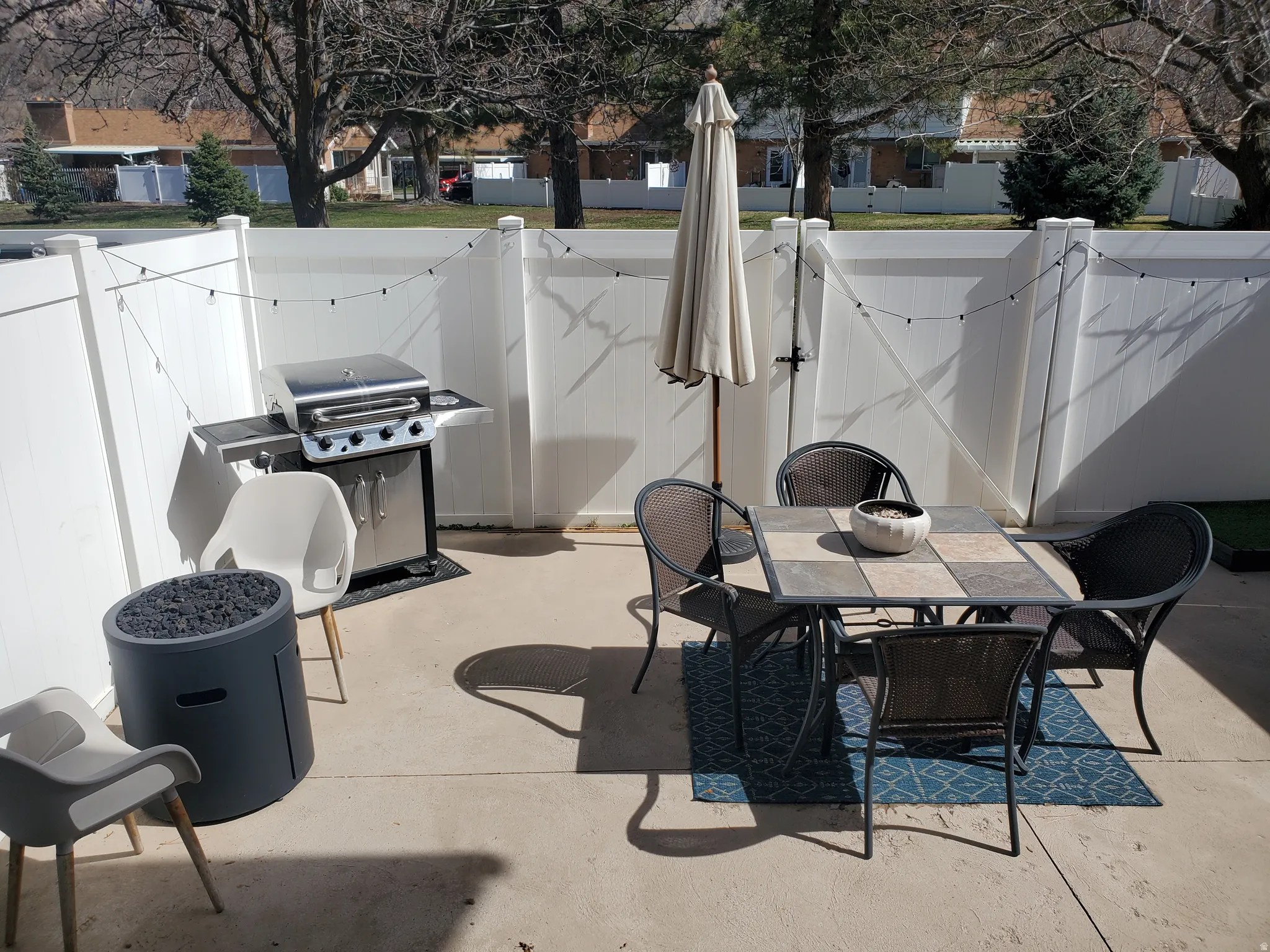 Paved patio area featuring privacy fencing, string lighting, and a square tile-top table