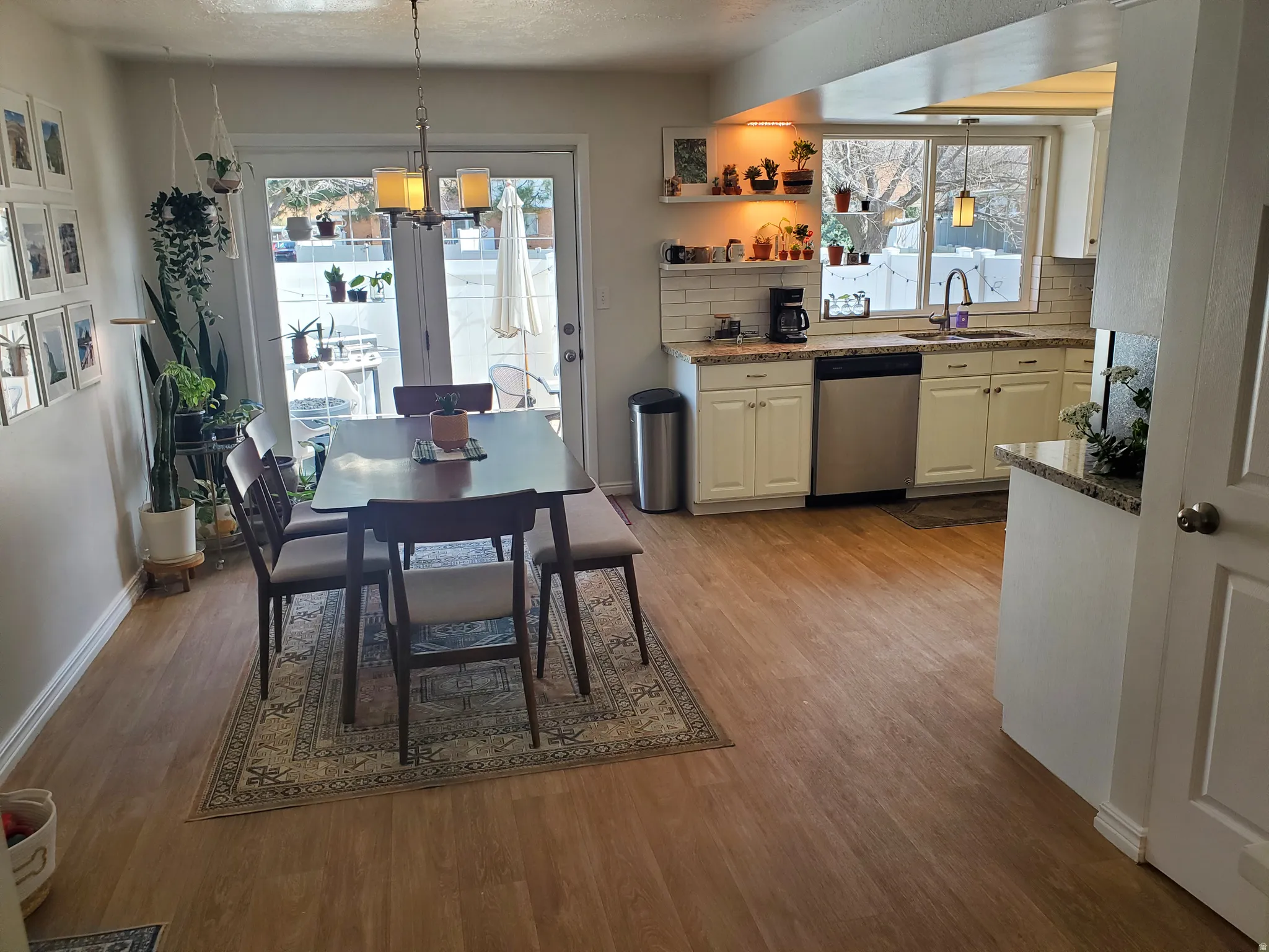 Open-concept living space featuring wood-finish flooring, a kitchen with white cabinetry and light-toned countertops, and a dining area with direct outdoor access via double glass doors
