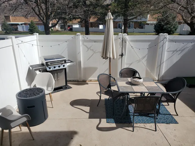 Paved patio area featuring privacy fencing, string lighting, and a square tile-top table