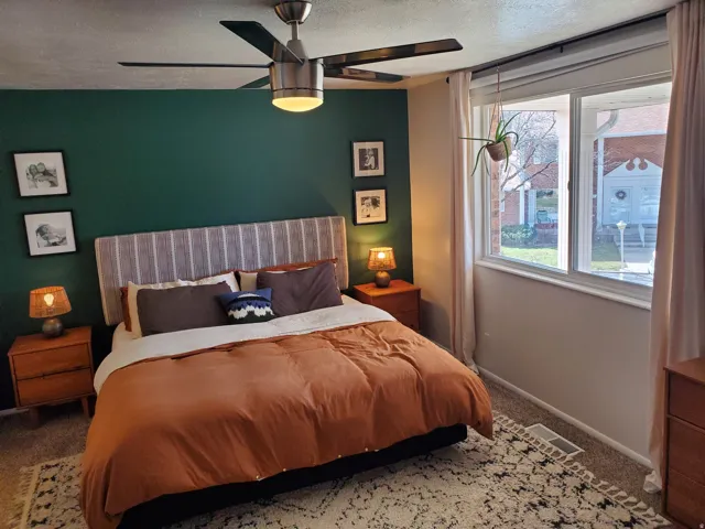 Bedroom featuring a ceiling fan with integrated lighting, a broad window providing ambient light, and carpeted flooring