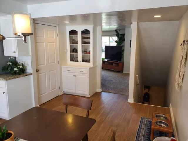 Hardwood-finish flooring extending from the dining area to a lower level, complemented by a built-in white display cabinet with glass-fronted upper doors and a functional white door