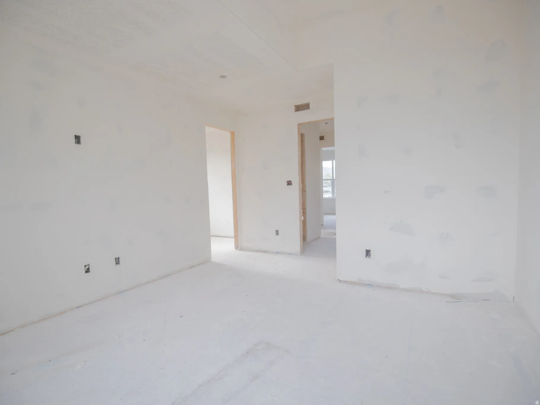 Unfinished interior space featuring white walls, open doorways, and multiple electrical outlets