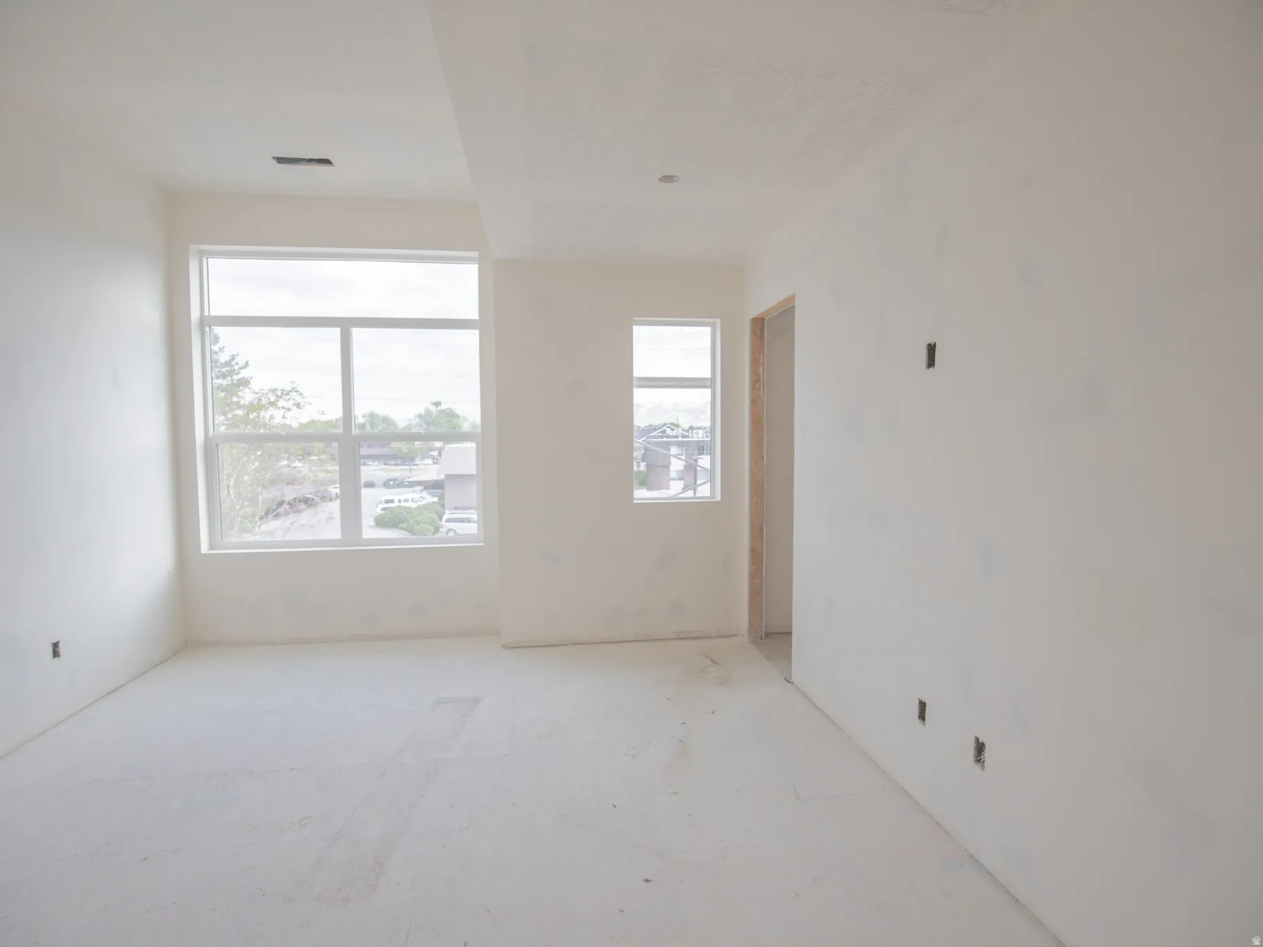 Spacious room featuring multiple windows, smooth white walls, high ceilings, and a framed doorway