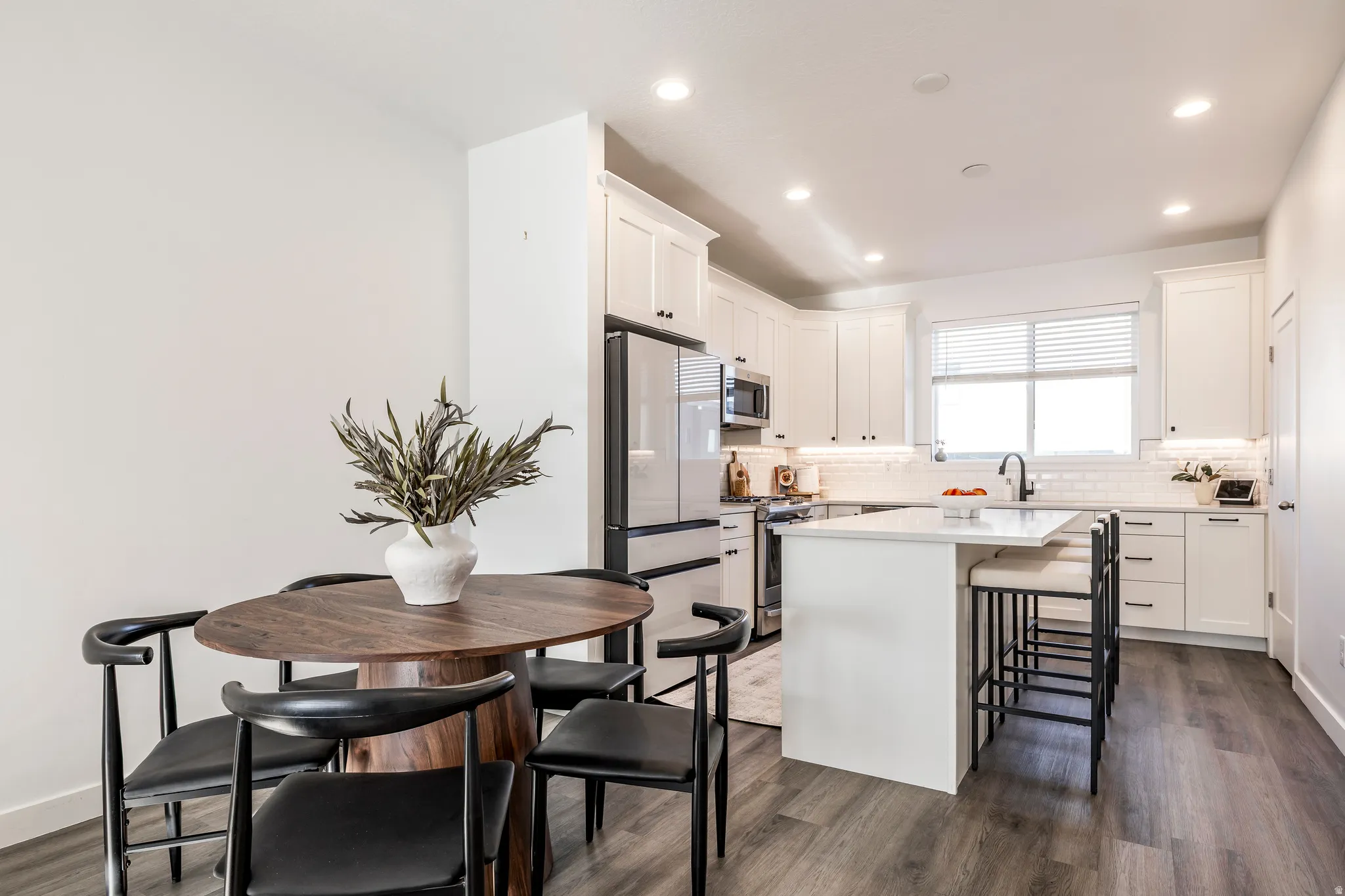 Modern kitchen featuring white cabinetry, a large kitchen island with seating, stainless steel appliances, a subway tile backsplash, and wood-finish flooring