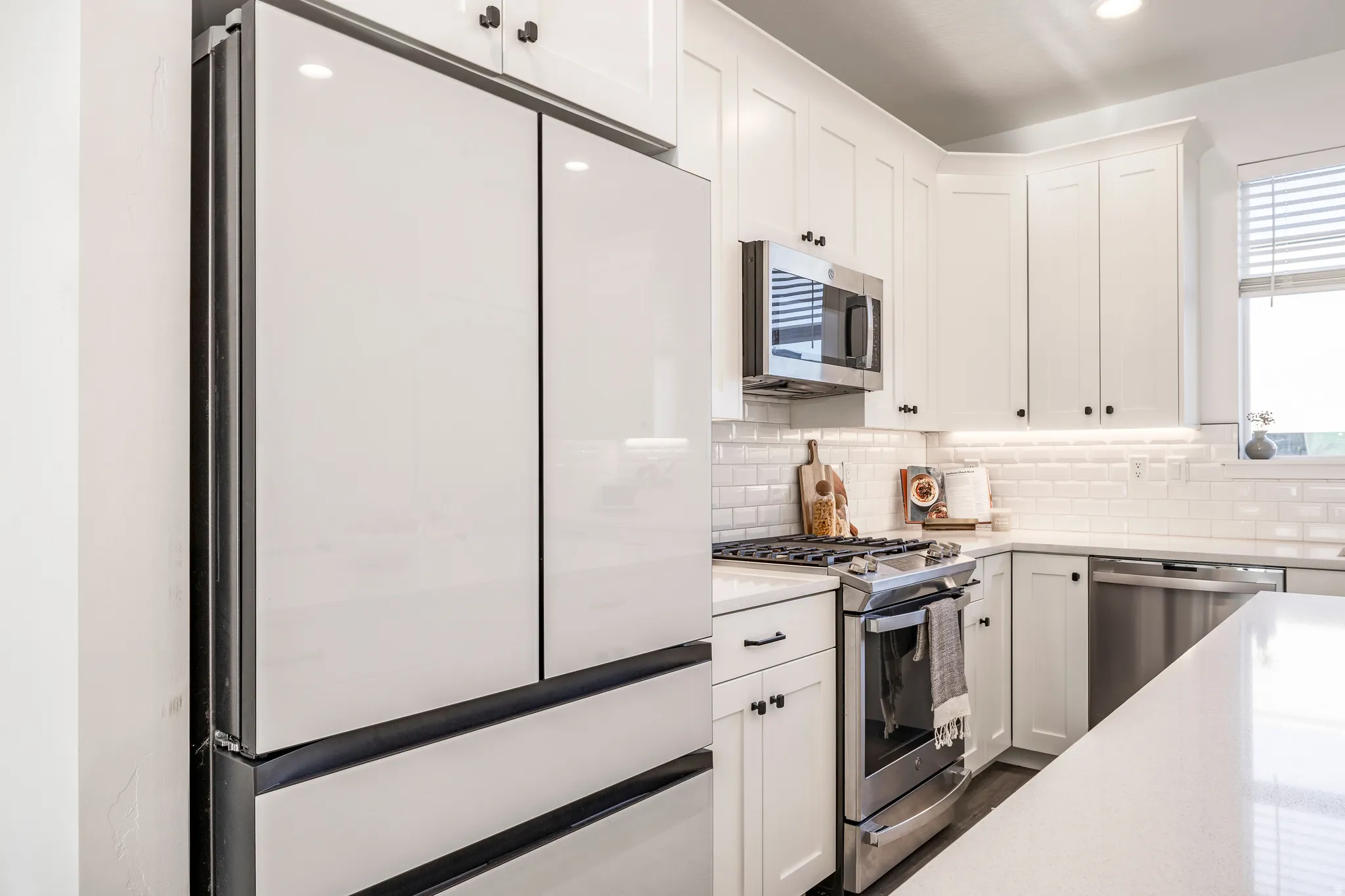Modern kitchen featuring a white French-door refrigerator, stainless steel appliances, white shaker cabinetry, white subway tile backsplash, and light-toned countertops