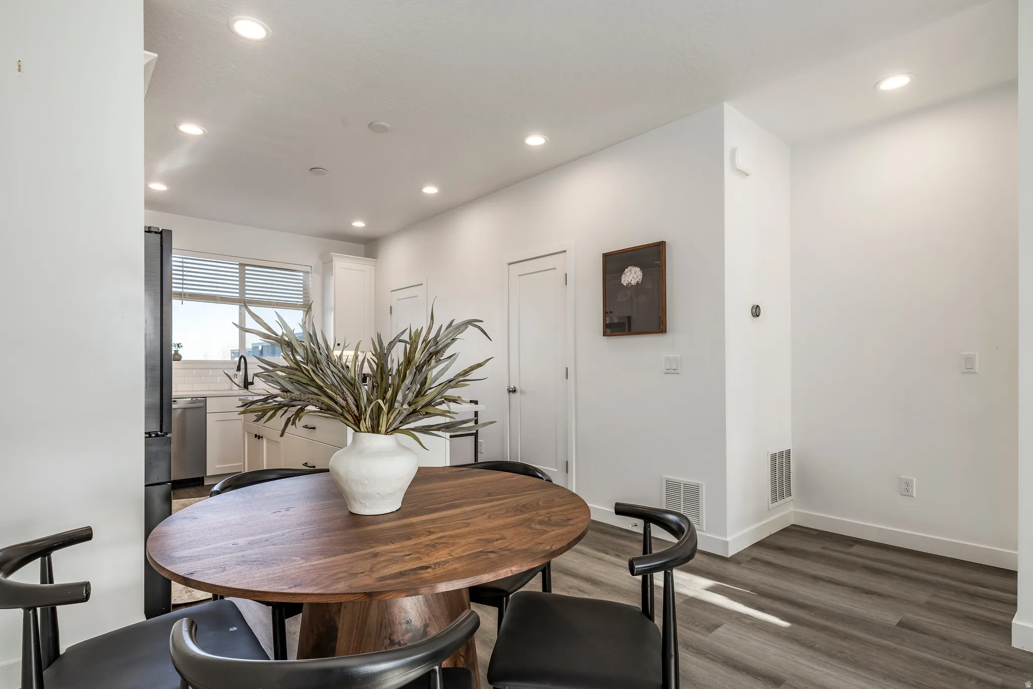 Contemporary kitchen and dining area featuring recessed lighting, wood-finish flooring, a white subway tile backsplash, and stainless steel appliances
