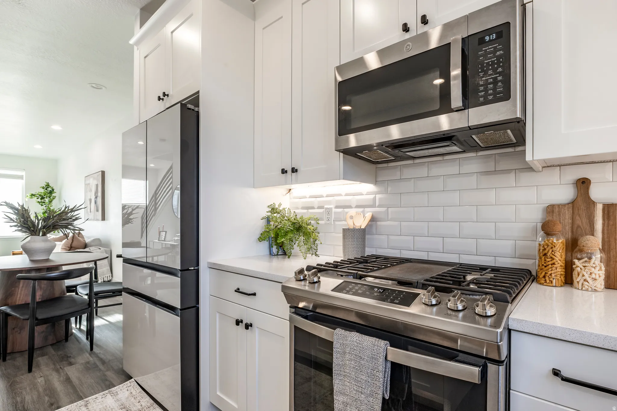 Modern kitchen featuring white shaker cabinetry, stainless steel appliances, a subway tile backsplash, light-toned countertops, and wood-finish flooring