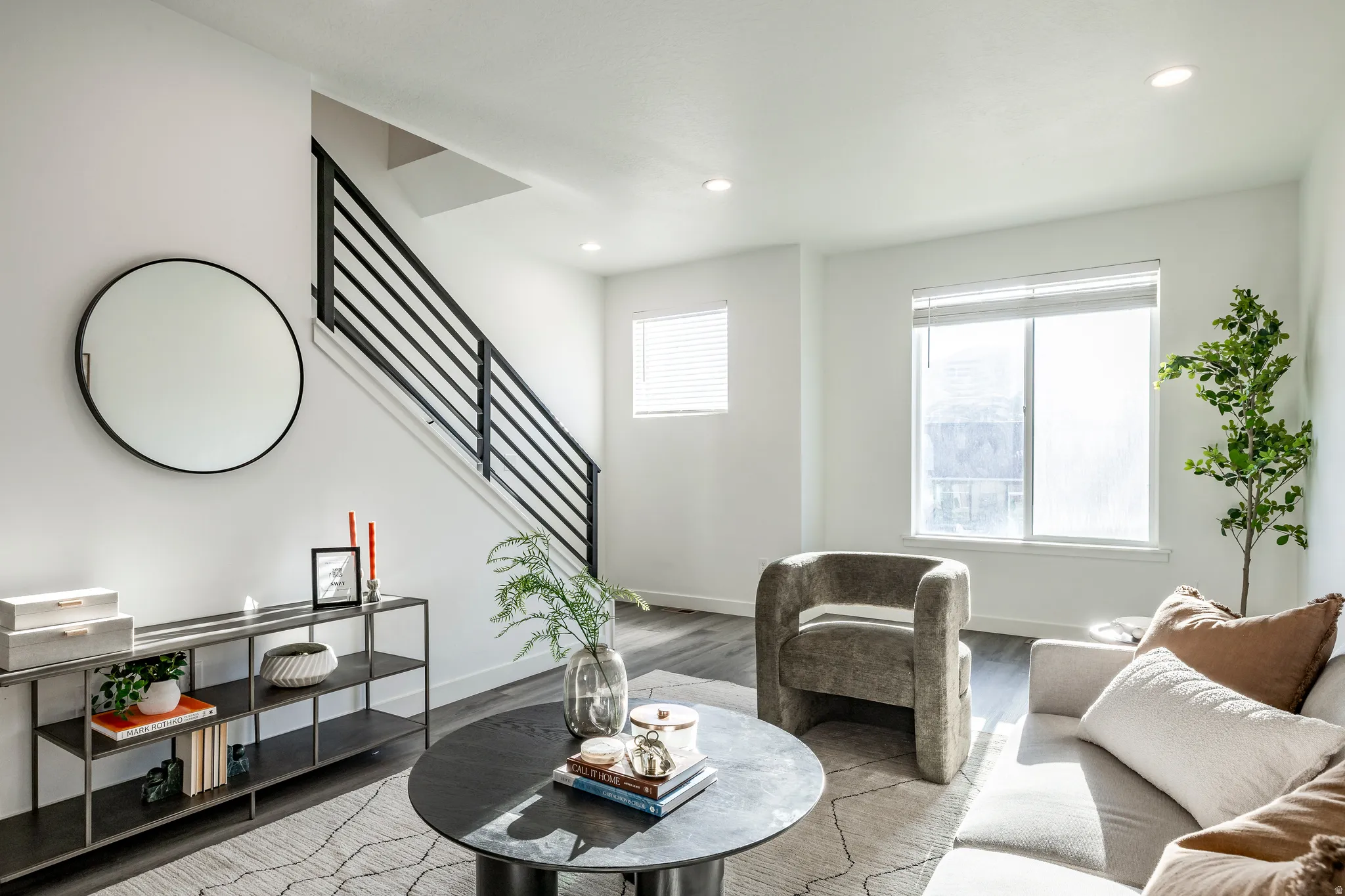 Contemporary living area featuring wood-finish flooring, recessed lighting, and a modern staircase with black metal railings