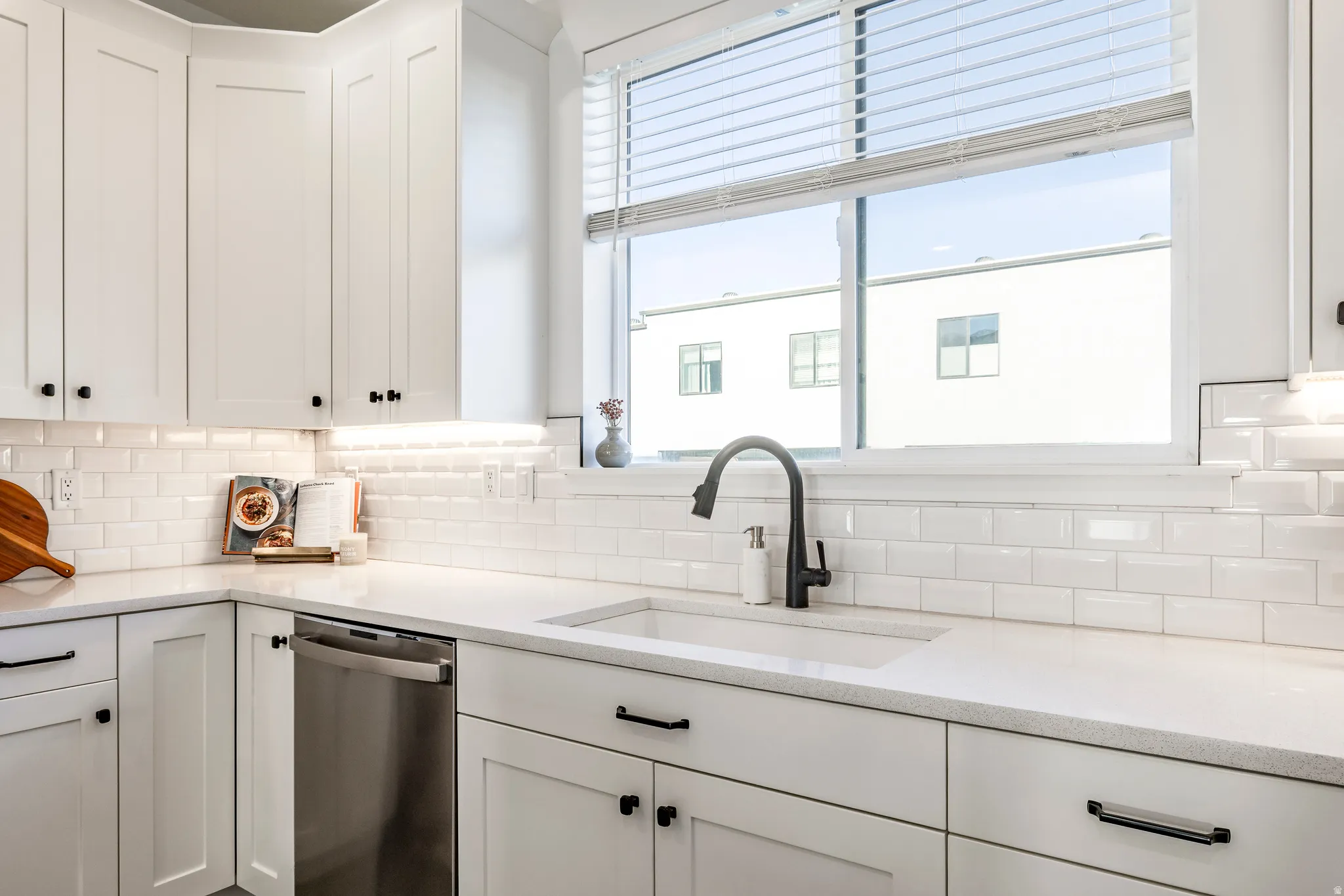 White kitchen featuring shaker-style cabinetry, quartz countertops, subway tile backsplash, and a stainless steel dishwasher