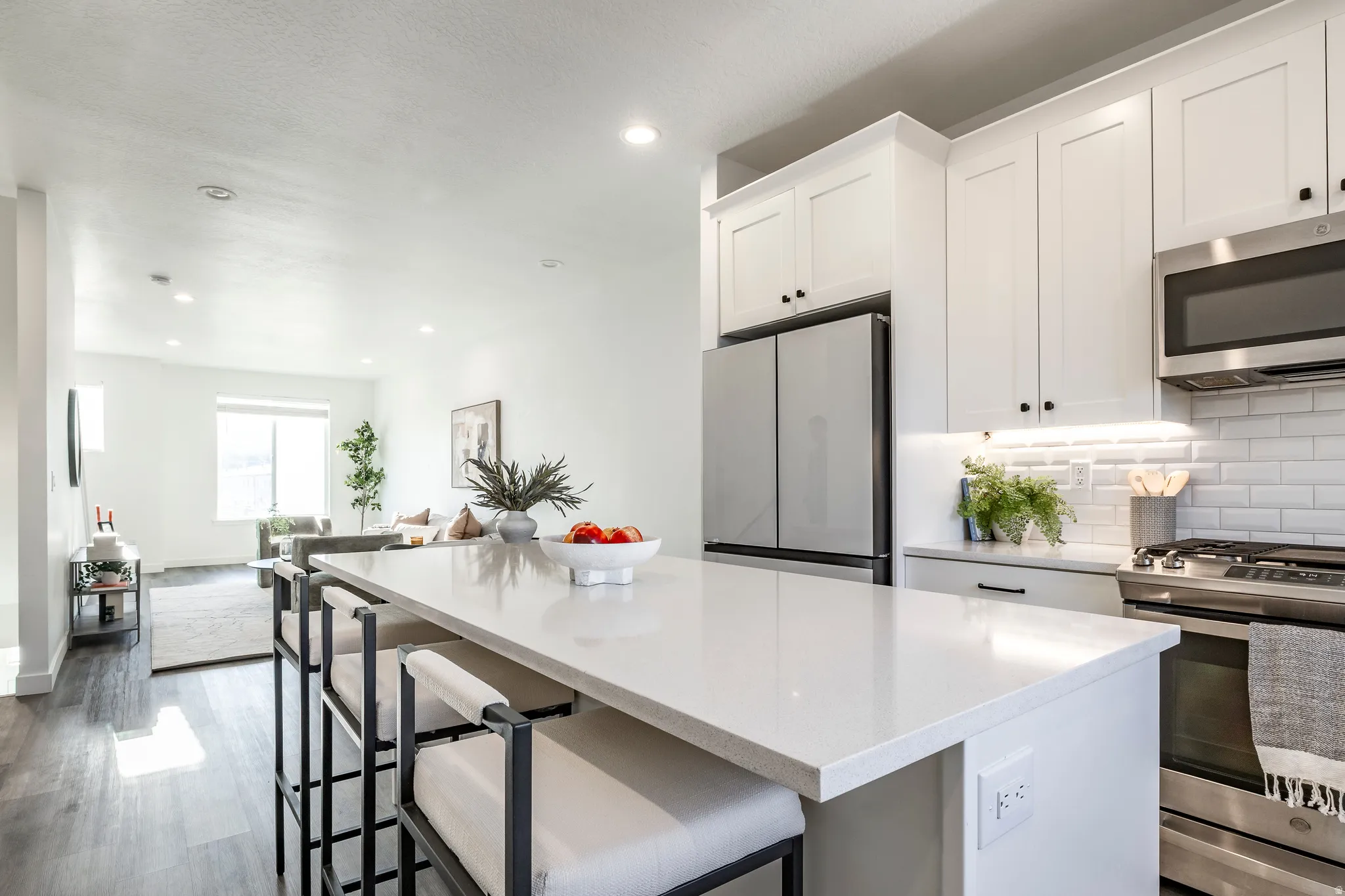 Kitchen island with a light-toned countertop, white cabinetry, stainless steel appliances, subway tile backsplash, and recessed lighting