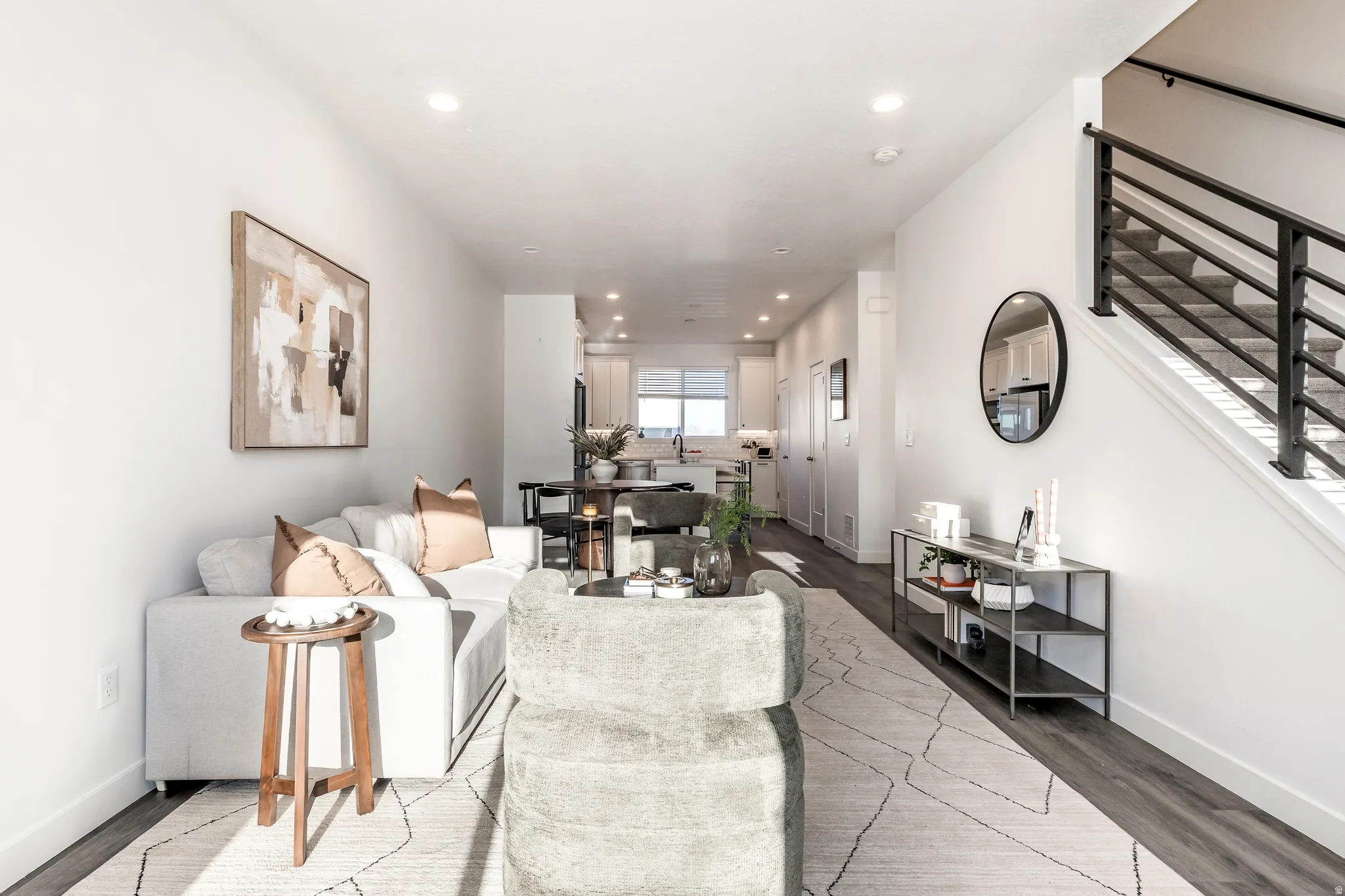 Open-concept living space featuring wood-finish flooring, recessed lighting, and a modern staircase with dark metal railings