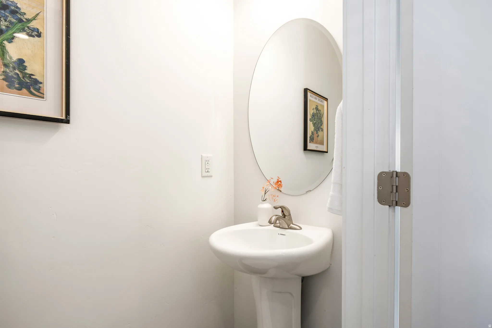 Pedestal sink with a polished chrome faucet and an oval mirror