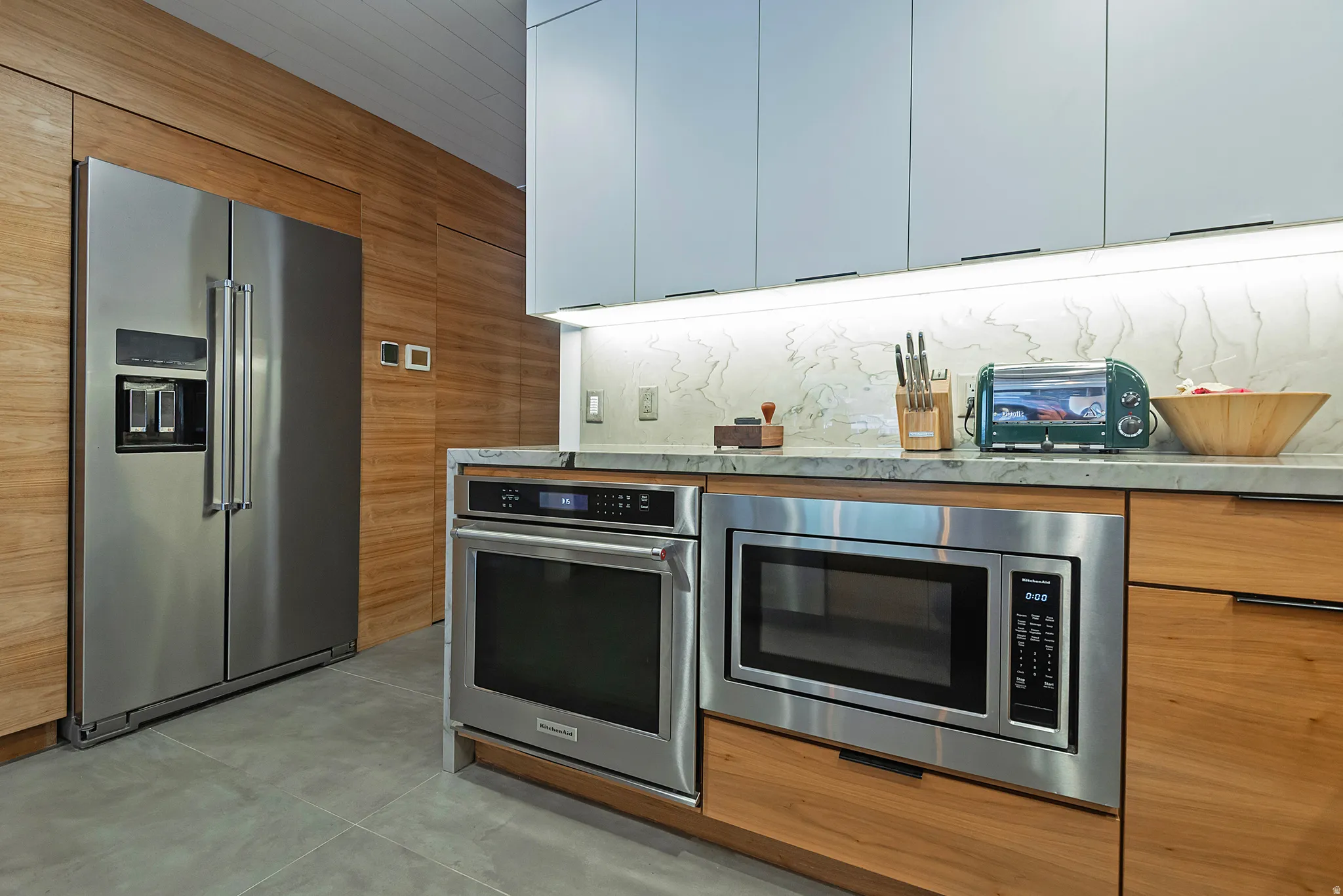 Modern kitchen featuring a stainless steel side-by-side refrigerator, built-in stainless steel microwave, and built-in stainless steel oven