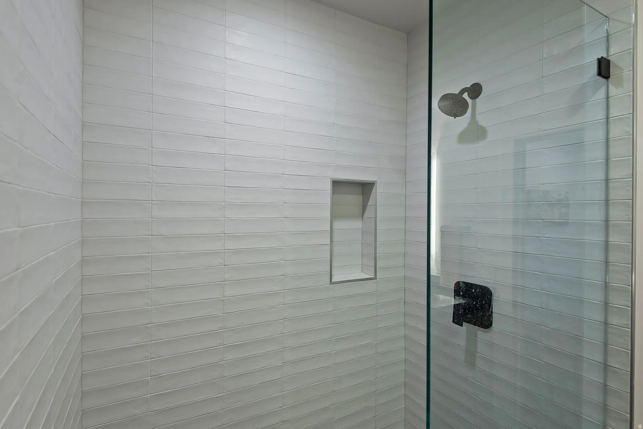 Glass-enclosed shower featuring horizontal white subway tile, an integrated shower niche, a dark bronze shower head, and a matching dark bronze shower handle