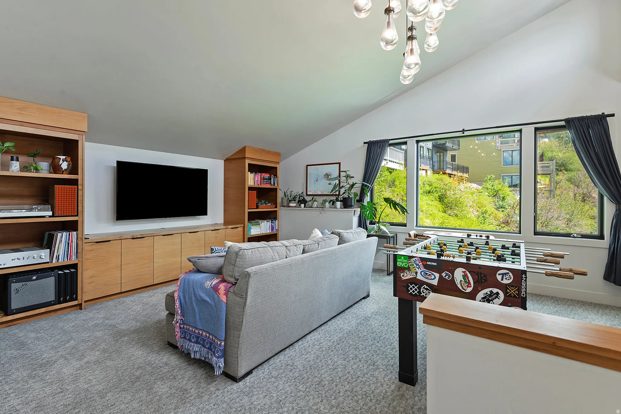 Vaulted ceiling room featuring light-toned built-in shelving and cabinetry, a large picture window, and gray carpet flooring