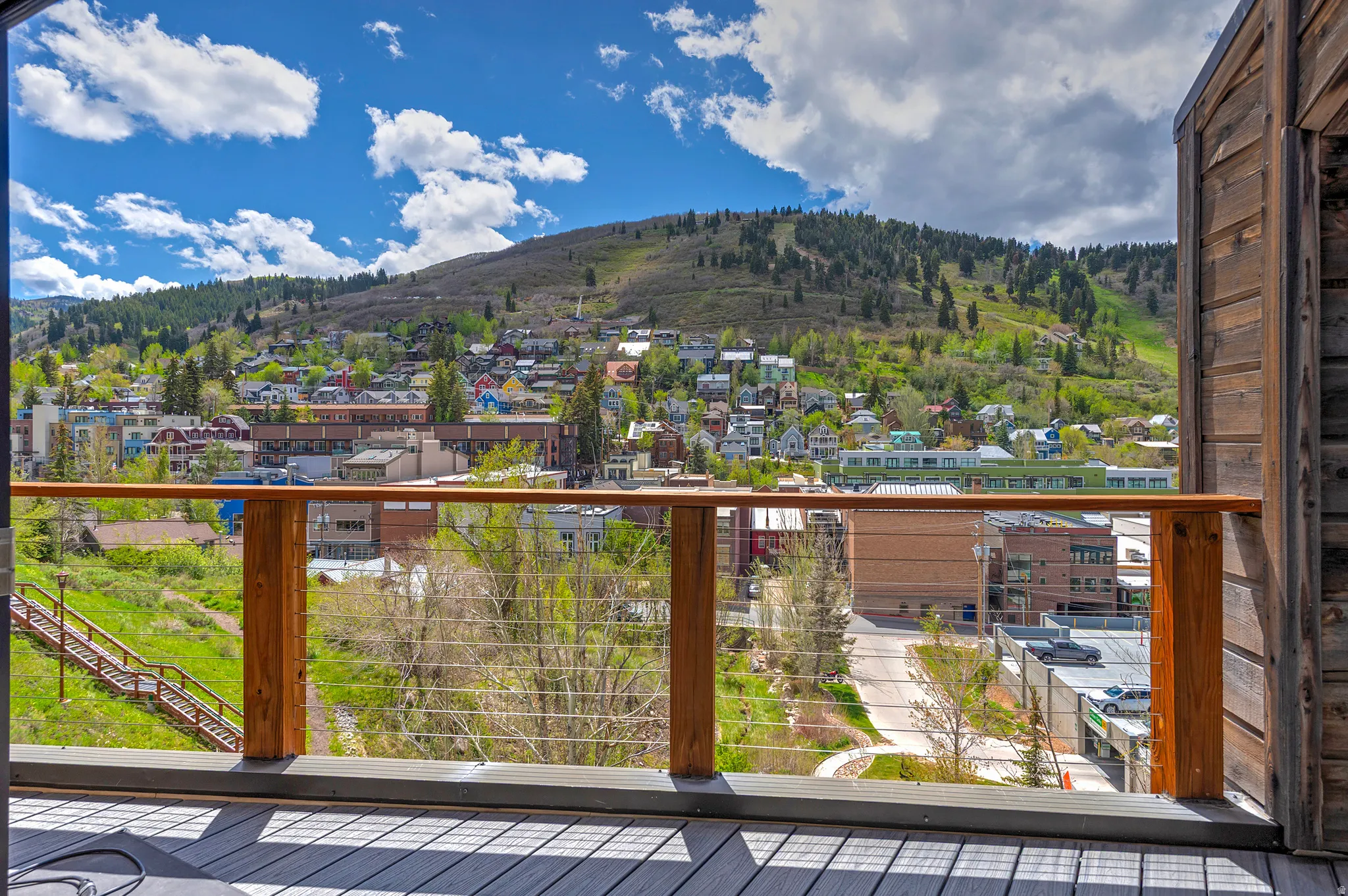 Deck with composite flooring and wood railing featuring cable infill, overlooking a mountain landscape with distant structures