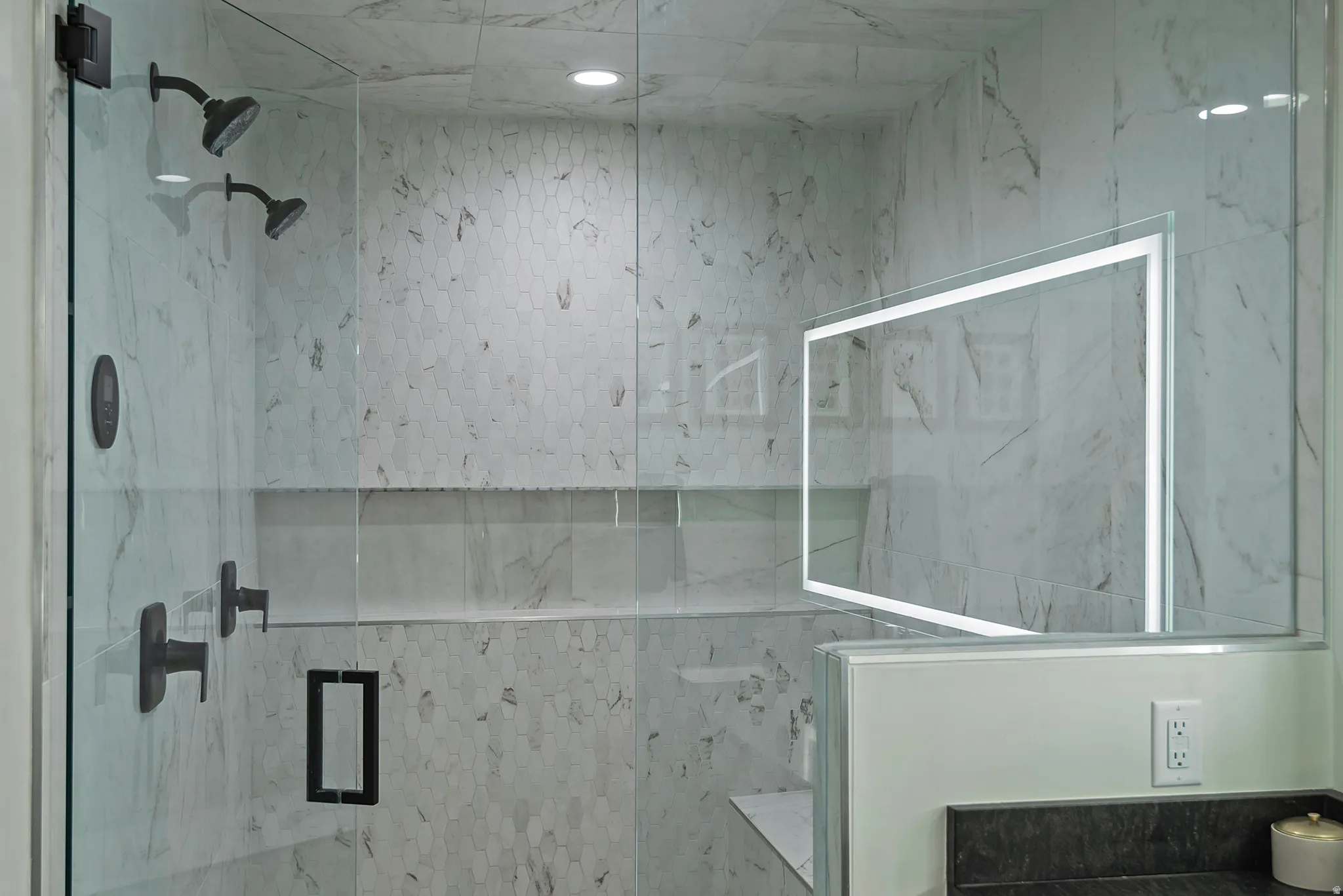 Glass-enclosed shower featuring dual matte black shower heads, white marble-look wall tiling, and a recessed product niche
