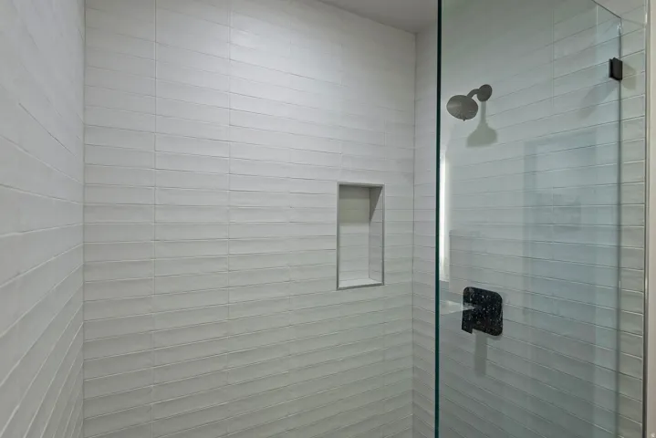 Glass-enclosed shower featuring horizontal white subway tile, an integrated shower niche, a dark bronze shower head, and a matching dark bronze shower handle