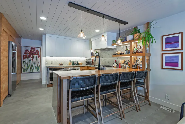 Spacious kitchen featuring a central island with bar seating, integrated shelving, under-cabinet lighting, panel-ready appliances, and a planked ceiling