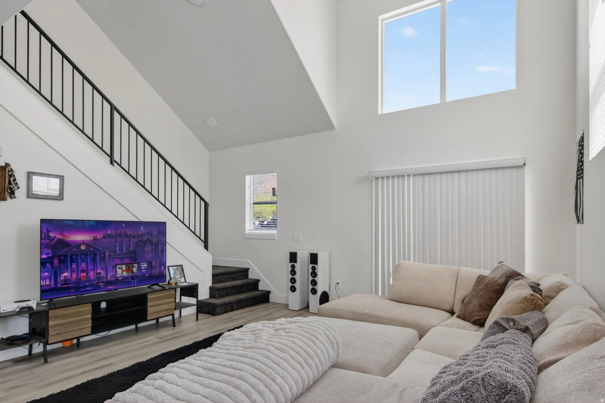 Two-story living area featuring high ceilings, light wood-finish flooring, and a contemporary black metal staircase railing