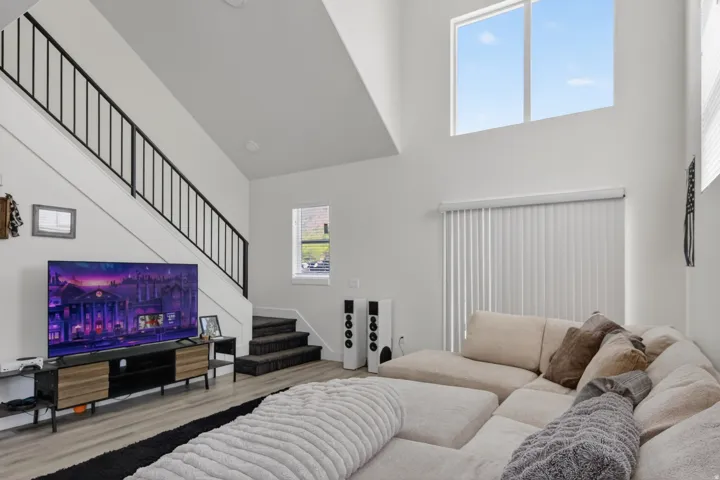 Two-story living area featuring high ceilings, light wood-finish flooring, and a contemporary black metal staircase railing