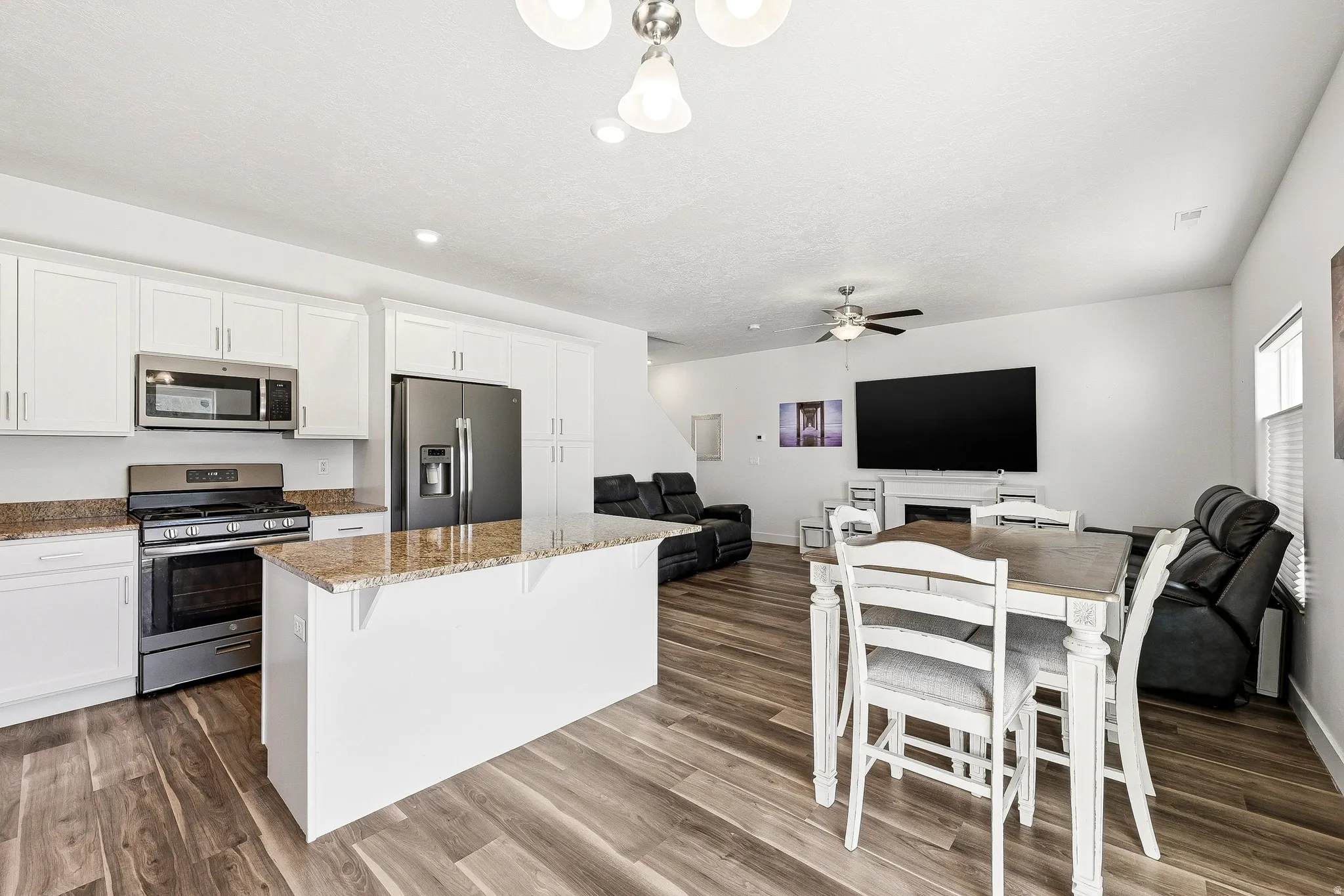 Open-concept living area with wood-finish flooring, a kitchen island with stone countertops, white shaker cabinetry, and stainless steel appliances