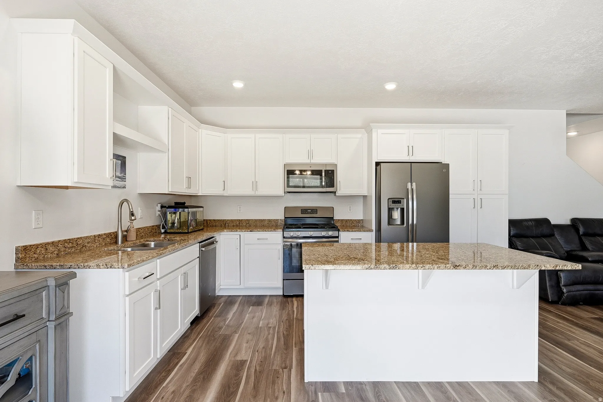 Modern kitchen featuring white cabinetry, granite countertops, stainless steel appliances, a center island with seating, and wood-finish flooring