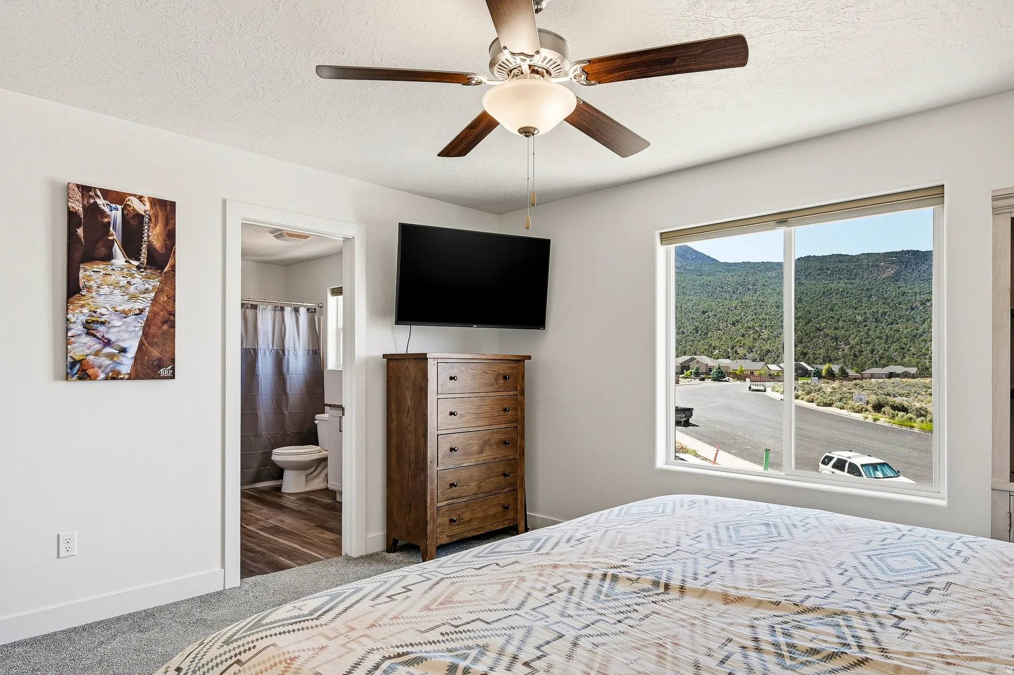 Spacious bedroom with a ceiling fan, carpet flooring, and a large window offering mountain scenery