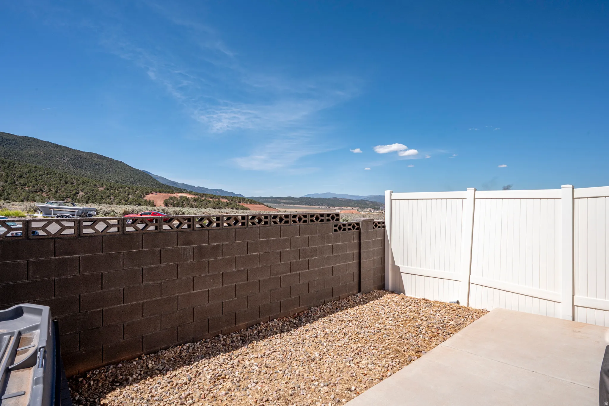 Outdoor space featuring a concrete patio, gravel landscaping, and a combination of block and white vinyl fencing