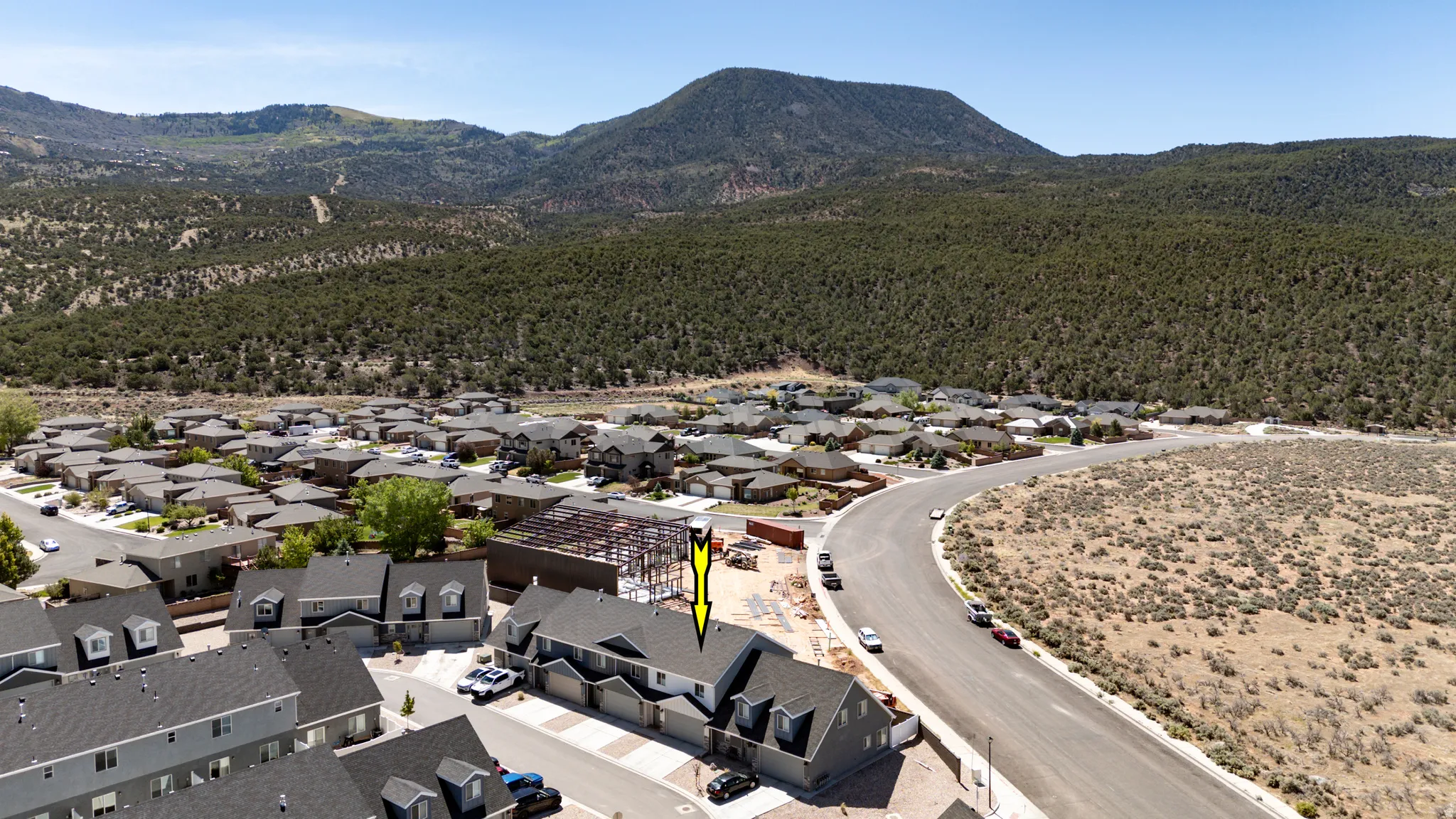 Aerial perspective of a multi-unit property within a residential development, featuring a mountain backdrop with extensive tree cover