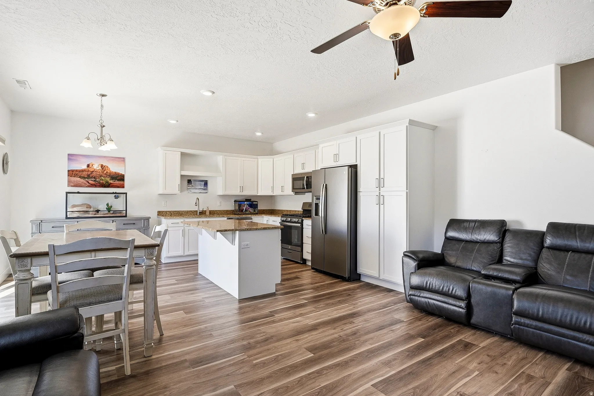 Open-concept living area featuring wood-finish flooring, white cabinetry, granite-look countertops, and stainless-steel appliances