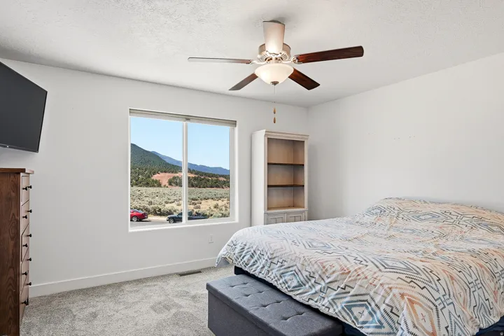 Spacious room with plush gray carpeting, a large window showcasing mountain scenery, a ceiling fan with integrated lighting, and a built-in shelving unit