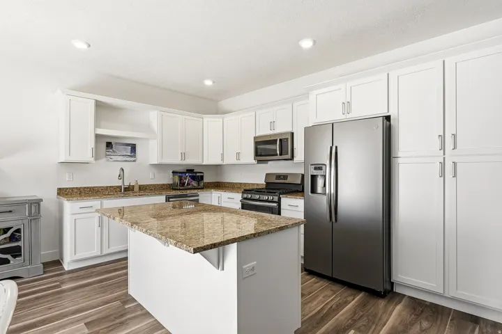 Kitchen featuring white cabinetry, wood-finish flooring, stainless steel appliances, and a central island with a stone-look countertop