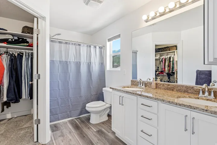 Bright bathroom featuring a dual vanity with granite-finish countertop, white cabinetry, and wood-finish flooring