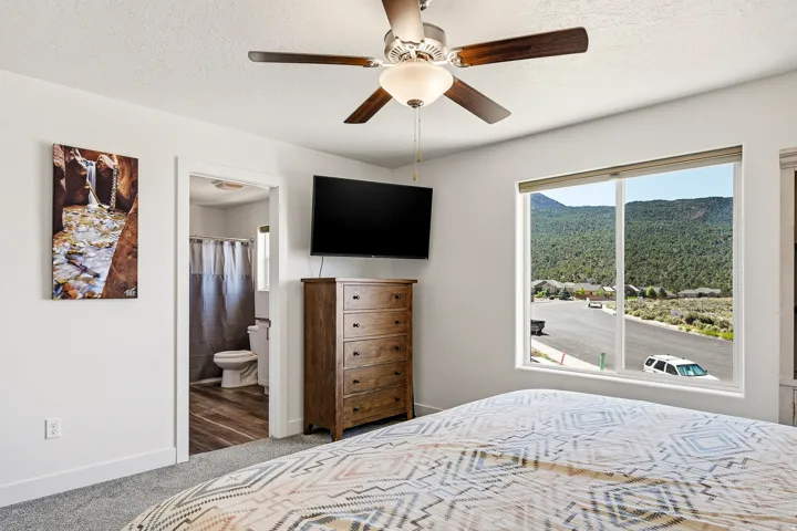 Spacious bedroom with a ceiling fan, carpet flooring, and a large window offering mountain scenery