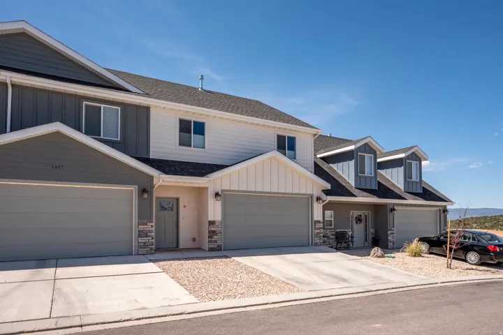 Multi-level townhome exterior featuring an attached two-car garage, stone veneer accents, vertical and horizontal siding, and dormer windows