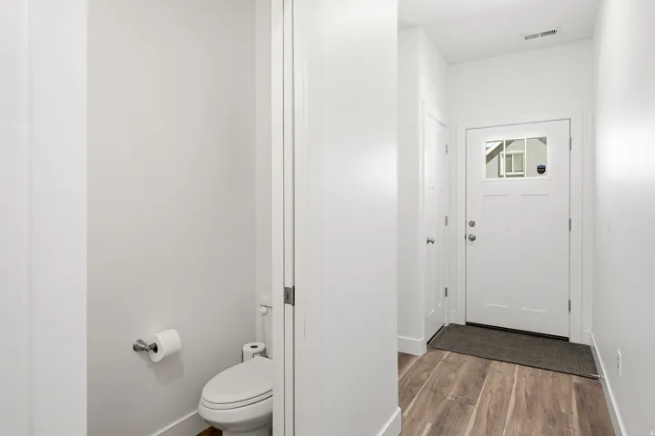 Entryway featuring wood-finish flooring, a white paneled door with decorative glass, and a discrete powder room with a white toilet