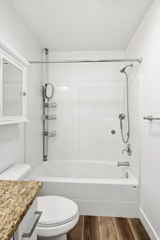 Bathroom featuring a white tub and shower combination, wood-finish flooring, a white vanity with a granite-look countertop, and a white medicine cabinet