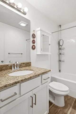 Vanity featuring a stone countertop with an undermount sink, white cabinetry with brushed nickel hardware, and a chrome faucet